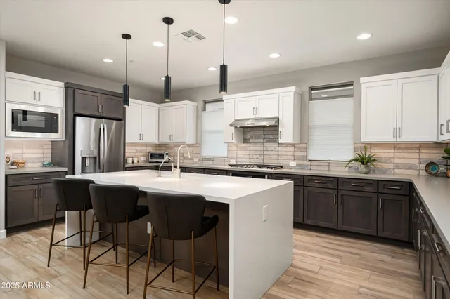 a kitchen with stainless steel appliances granite countertop a sink a stove a refrigerator and island with wooden floor