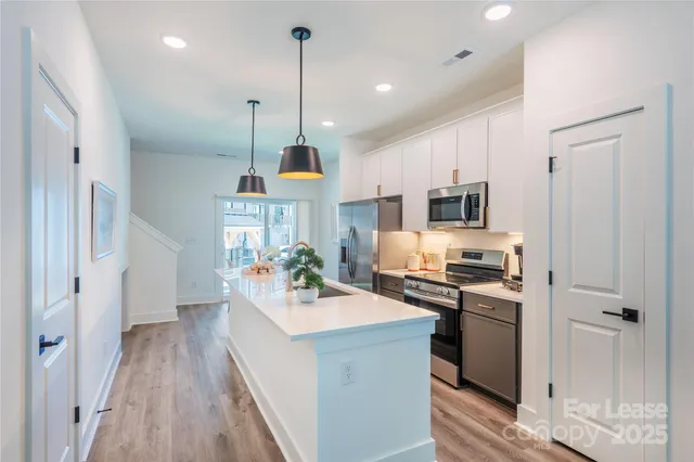 a kitchen with stainless steel appliances a stove a sink dishwasher a refrigerator white cabinets and wooden floor with floors