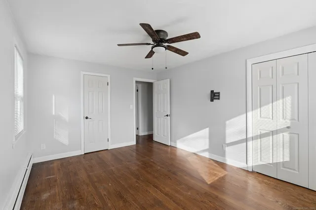 a view of an empty room with wooden floor and a ceiling fan