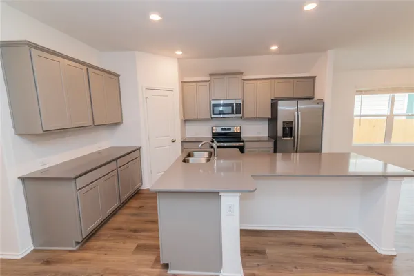 a kitchen with stainless steel appliances granite countertop a sink a stove a refrigerator a microwave a sink and white cabinets with wooden floor