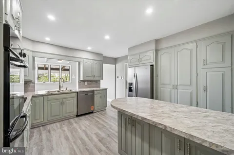 a kitchen with stainless steel appliances granite countertop a refrigerator a sink dishwasher a stove and white countertops with wooden floor