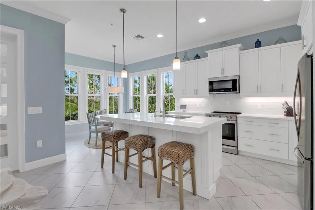 6509 Dominica Drive, Unit 101 Naples, FL 34113 - Photo 3 of 33 a kitchen with kitchen island granite countertop a table chairs microwave and refrigerator