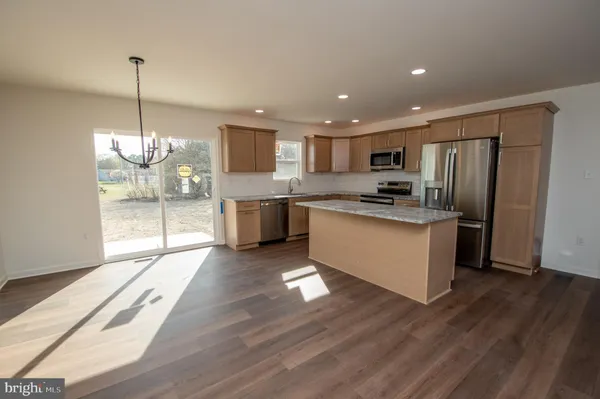 a kitchen with stainless steel appliances granite countertop a refrigerator a sink dishwasher a stove and a dining table with wooden floor