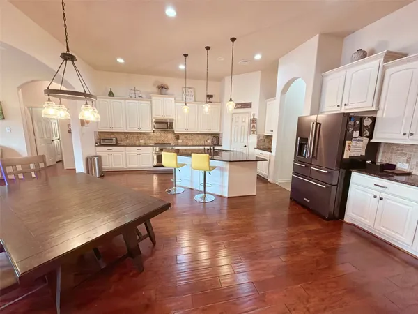 a large kitchen with stainless steel appliances kitchen island granite countertop a stove a refrigerator a sink a dining table and chairs with wooden floor
