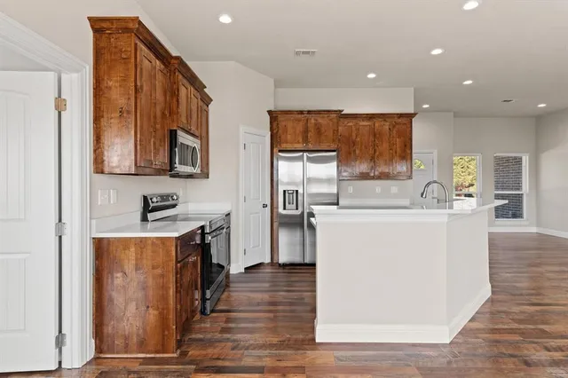 a kitchen with stainless steel appliances granite countertop a stove top oven a sink a refrigerator and white cabinets with wooden floor