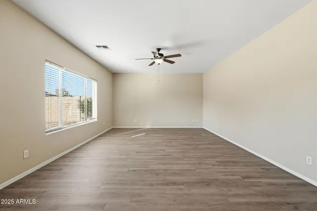 a view of an empty room with wooden floor and a ceiling fan