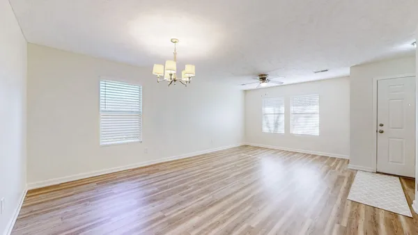 an empty room with wooden floor chandelier and windows