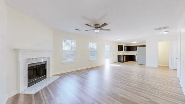 an empty room with wooden floor a ceiling fan a fireplace and windows