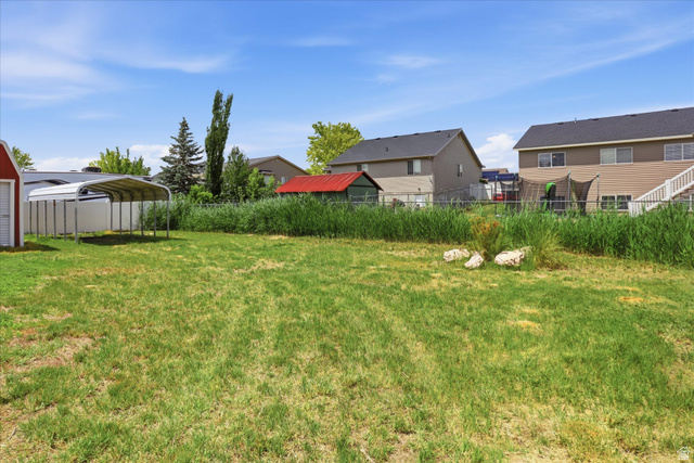 3636 West 910 South Syracuse, UT 84075 - Photo 63 of 70 Expansive grass yard with a metal carport structure and a red-roofed shed
