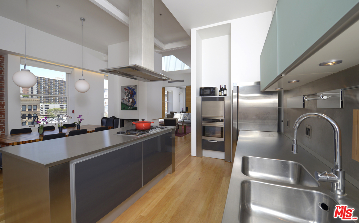 257 South Spring Street, Unit PHMN Los Angeles, CA 90012 - Photo 5 of 17 a kitchen with stainless steel appliances kitchen island granite countertop a refrigerator a sink a stove and a refrigerator with wooden floor