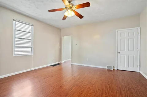 an empty room with wooden floor chandelier fan and windows