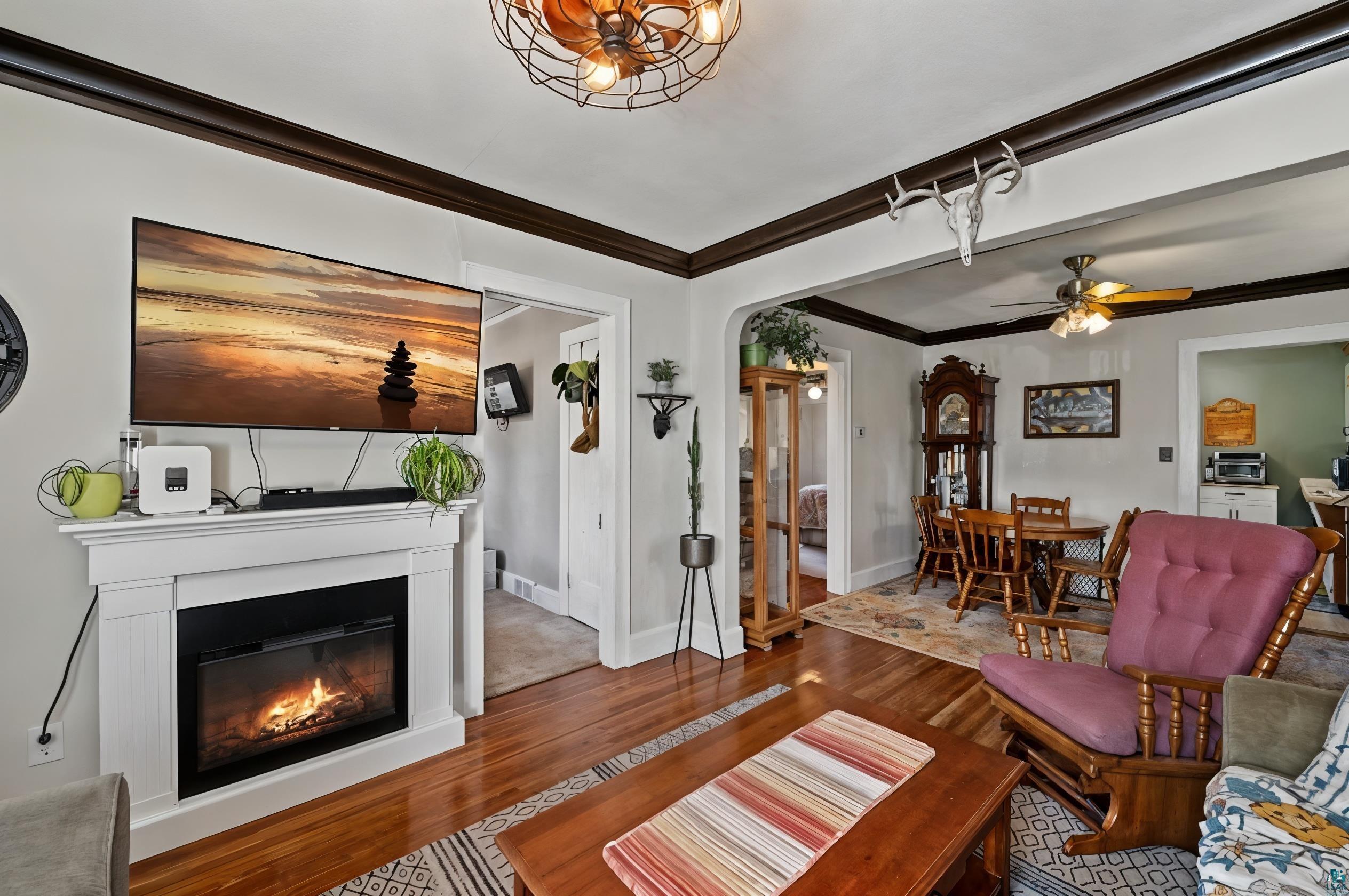 3209 Chestnut Street Duluth, MN 55806 - Photo 6 of 28 Hardwood flooring in a living space featuring a white mantel fireplace, dark crown molding, and an arched doorway leading to an additional room