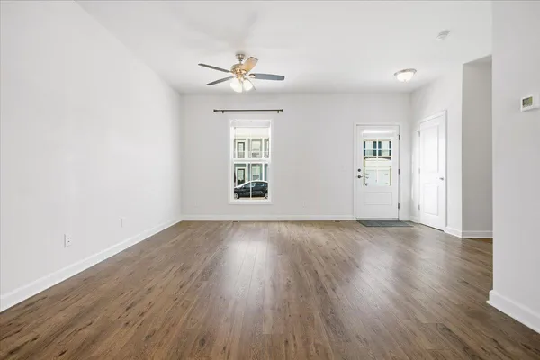 an empty room with wooden floor chandelier fan and windows