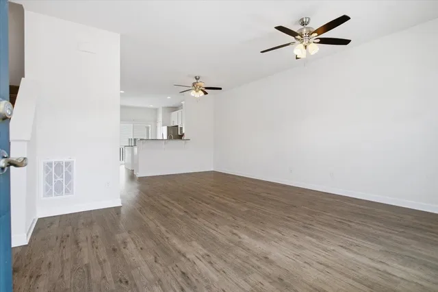 a view of an empty room with wooden floor and a ceiling fan