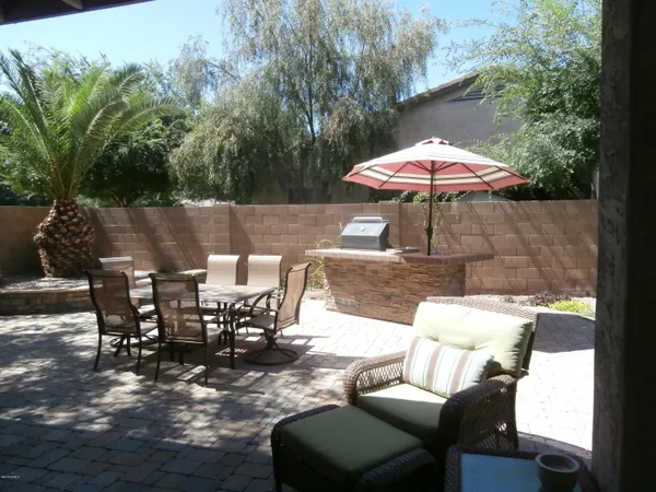 a view of a patio with a dining table and chairs under an umbrella with barbeque grill and wooden fence