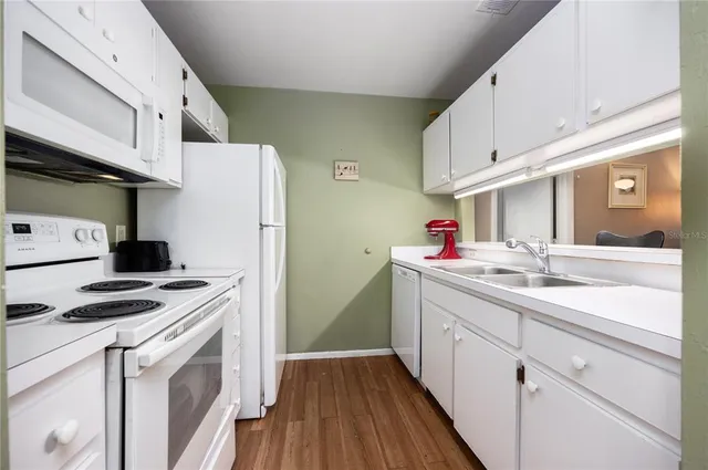 a kitchen with a sink dishwasher stove and white cabinets with wooden floor