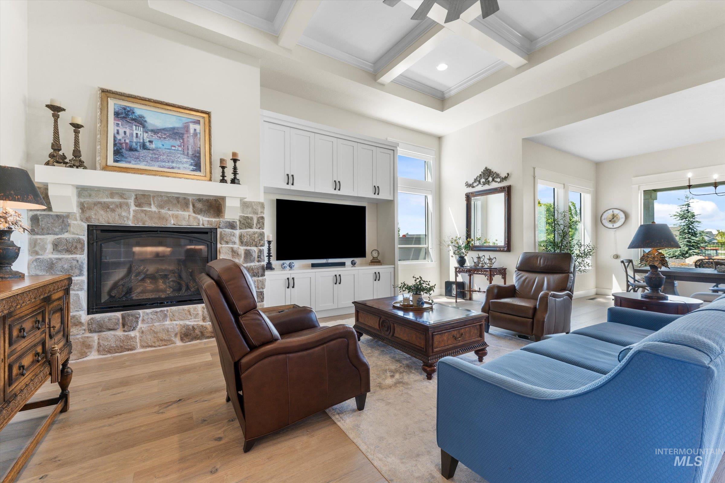 6585 South Pemberley Way Meridian, ID 83642 - Photo 9 of 43 Spacious living area featuring a stone-clad fireplace with a white mantel, custom built-in cabinetry, wood-finish flooring, a tray ceiling, and ample natural light from multiple windows