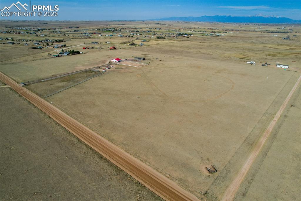 7880 J D Johnson Road Peyton, CO 80831 - Photo 27 of 50 Expansive rural acreage featuring a red-roofed structure, several outbuildings, and a dirt road