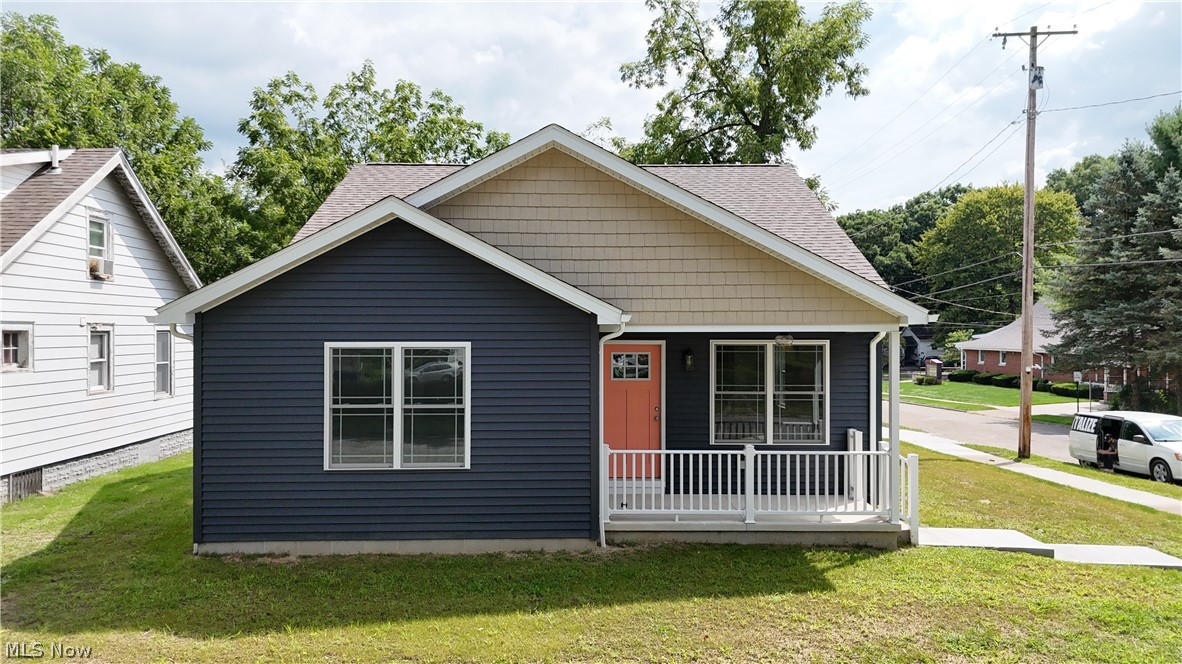 78 Prospect Street Struthers, OH 44471 - Photo 1 of 17 Single-story residence featuring a covered front porch with white railing, a vibrant coral entry door, and dark blue horizontal siding
