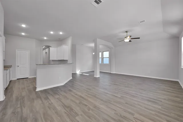a view of an empty room and kitchen with wooden floor