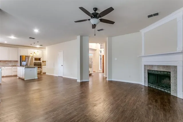 a view of an empty room with wooden floor and a kitchen