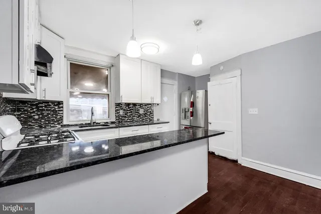 a kitchen with granite countertop a stove a sink and white cabinets with wooden floor