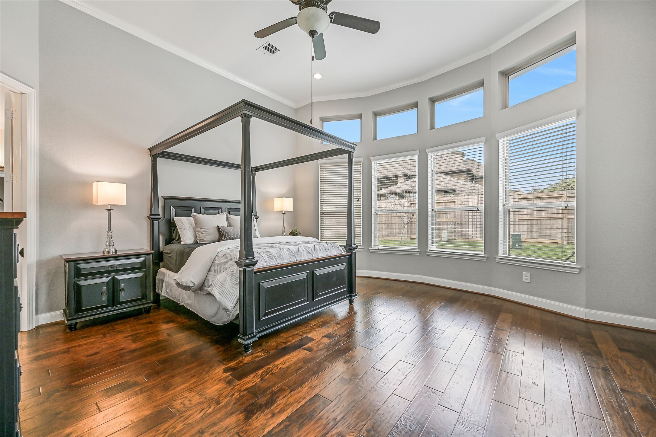 1008 Point Isabel Lane Friendswood, TX 77546 - Photo 28 of 50 A spacious and serene primary retreat showcases rich wood flooring, an elevated 12-foot ceiling trimmed with crown molding, and a wall of windows topped with transoms that flood the room with natural light while maintaining privacy.