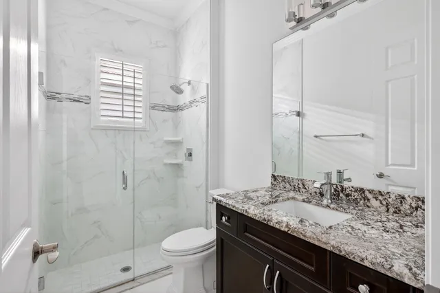 a bathroom with a granite countertop sink a toilet a shower and a mirror