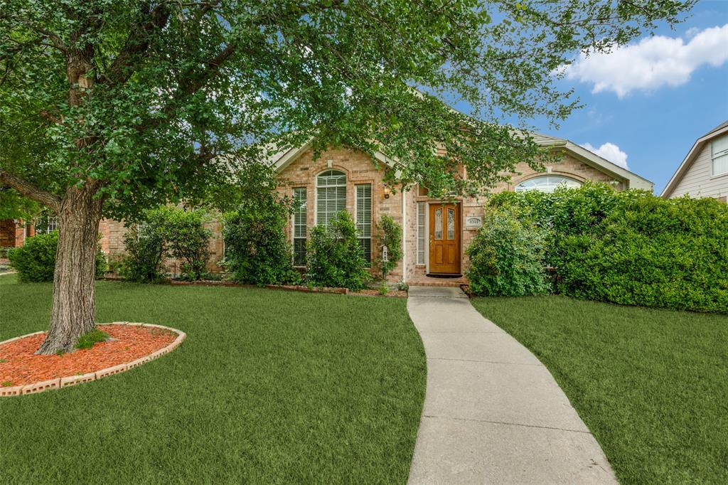 View of property hidden behind natural elements featuring brick siding and a front lawn