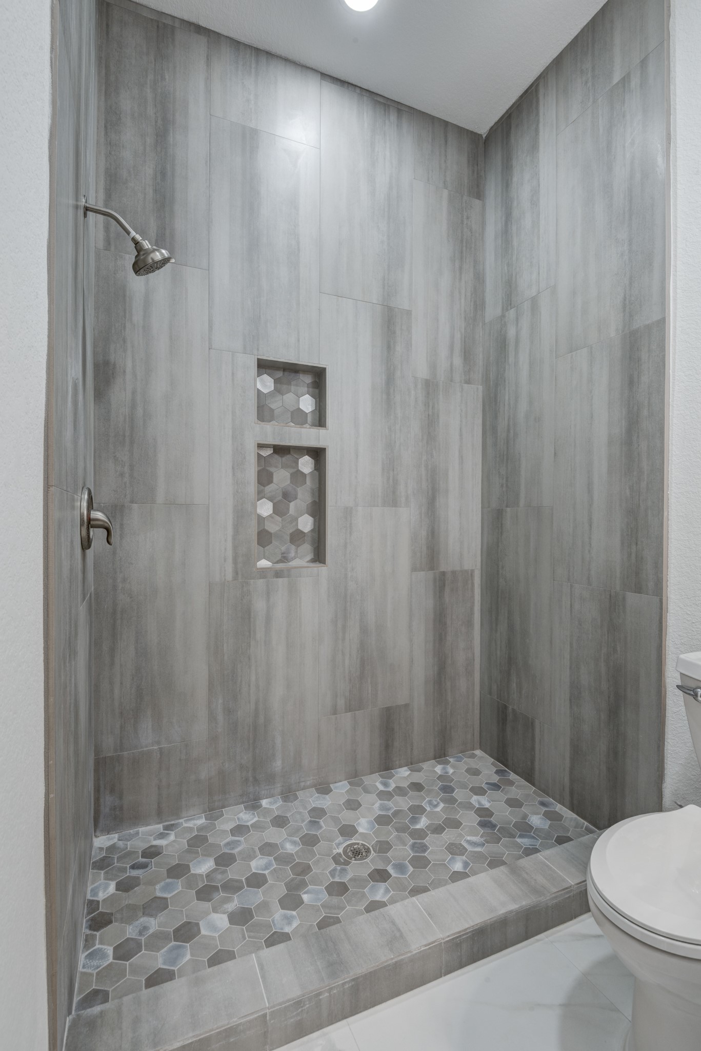 7348 Love Road Fulshear, TX 77441 - Photo 24 of 48 Elegant walk-in shower with sleek gray tiles and a stylish hexagonal floor, featuring convenient recessed shelving.
