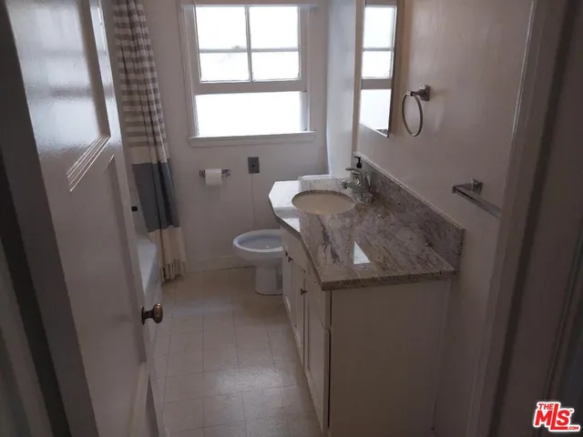 a bathroom with a granite countertop sink toilet and a window