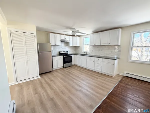 a kitchen with granite countertop a refrigerator oven a sink dishwasher and white cabinets with wooden floor