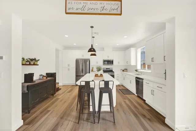 a dinning area with stainless steel appliances kitchen island granite countertop a stove a sink a dining table and chairs with wooden floor