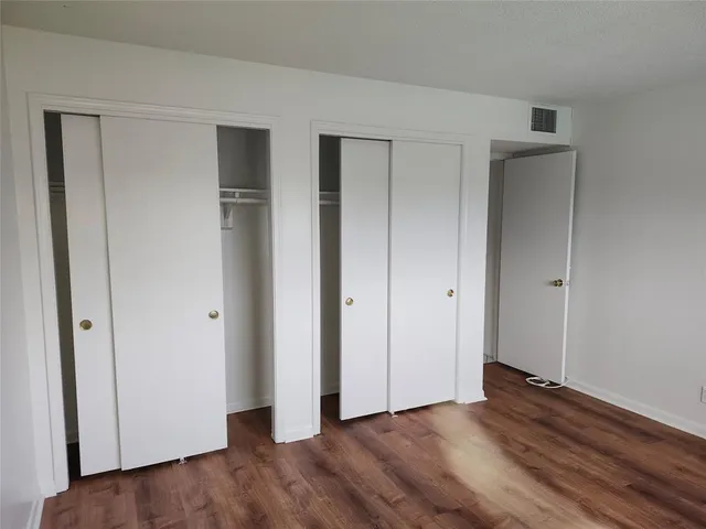 a view of an empty room with wooden floor and closet