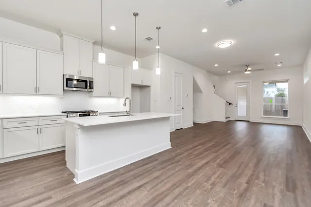 a open kitchen with stainless steel appliances granite countertop a stove a sink a refrigerator and white cabinets with wooden floor