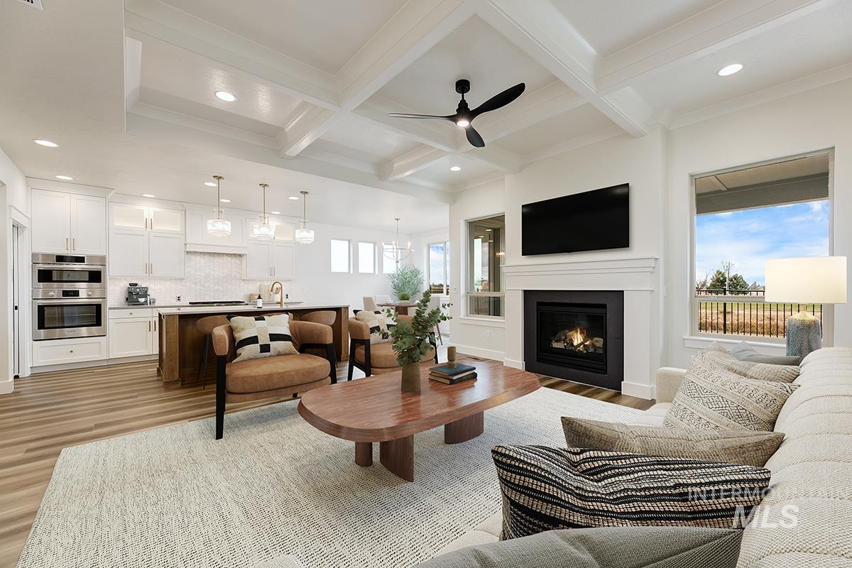 3281 East Englehart Lane Meridian, ID 83642 - Photo 4 of 35 Living room featuring ceiling fan, coffered ceiling, light wood-style flooring, a warm lit fireplace, and a chandelier