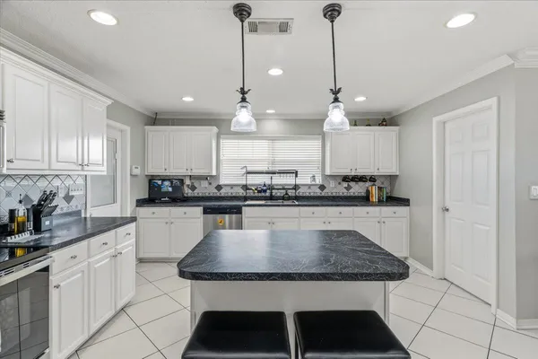 a kitchen with stainless steel appliances granite countertop a stove a sink a refrigerator white cabinets and couches with wooden floor