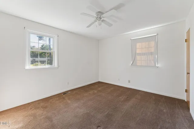 an empty room with a chandelier fan and windows