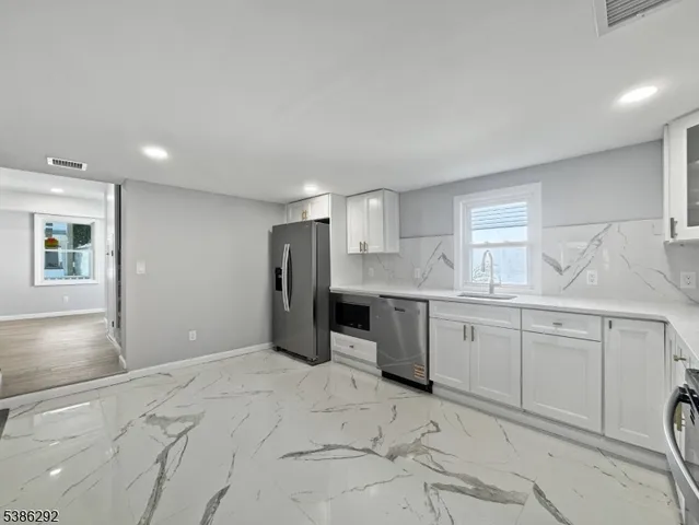 a large white kitchen with granite countertop a sink white cabinets and stainless steel appliances