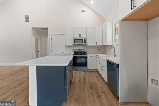 a kitchen with stainless steel appliances a sink dishwasher a stove top oven a refrigerator with white cabinets and wooden floor