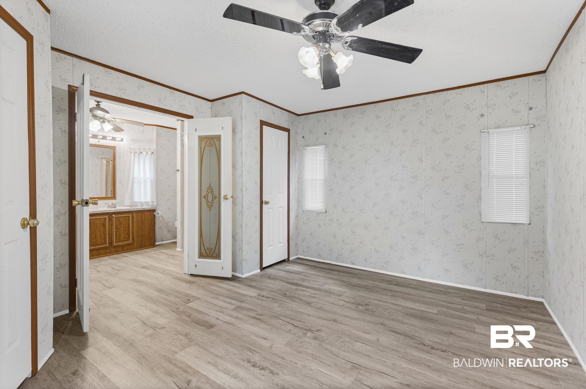 8675 Hunters Pointe Drive North Theodore, AL 36582 - Photo 10 of 20 Spacious room featuring wood-finish flooring, two windows with blinds, a ceiling fan with integrated lighting, and a doorway opening to an additional area with a vanity