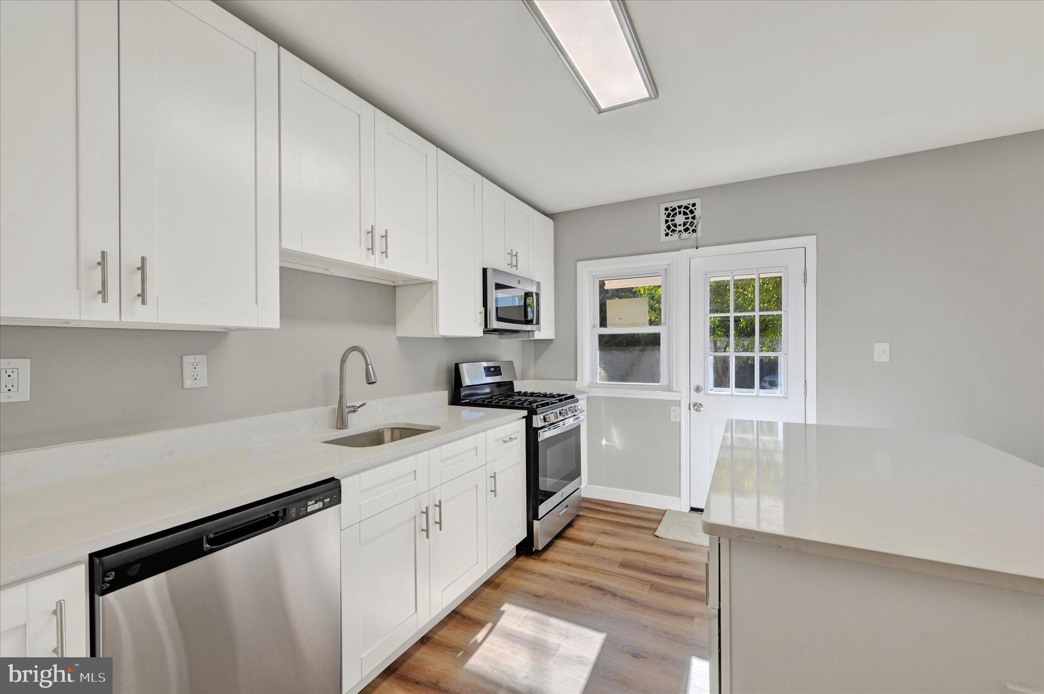 4811 Coleherne Road Baltimore, MD 21229 - Photo 10 of 28 a kitchen with a sink dishwasher a stove and white cabinets with wooden floor
