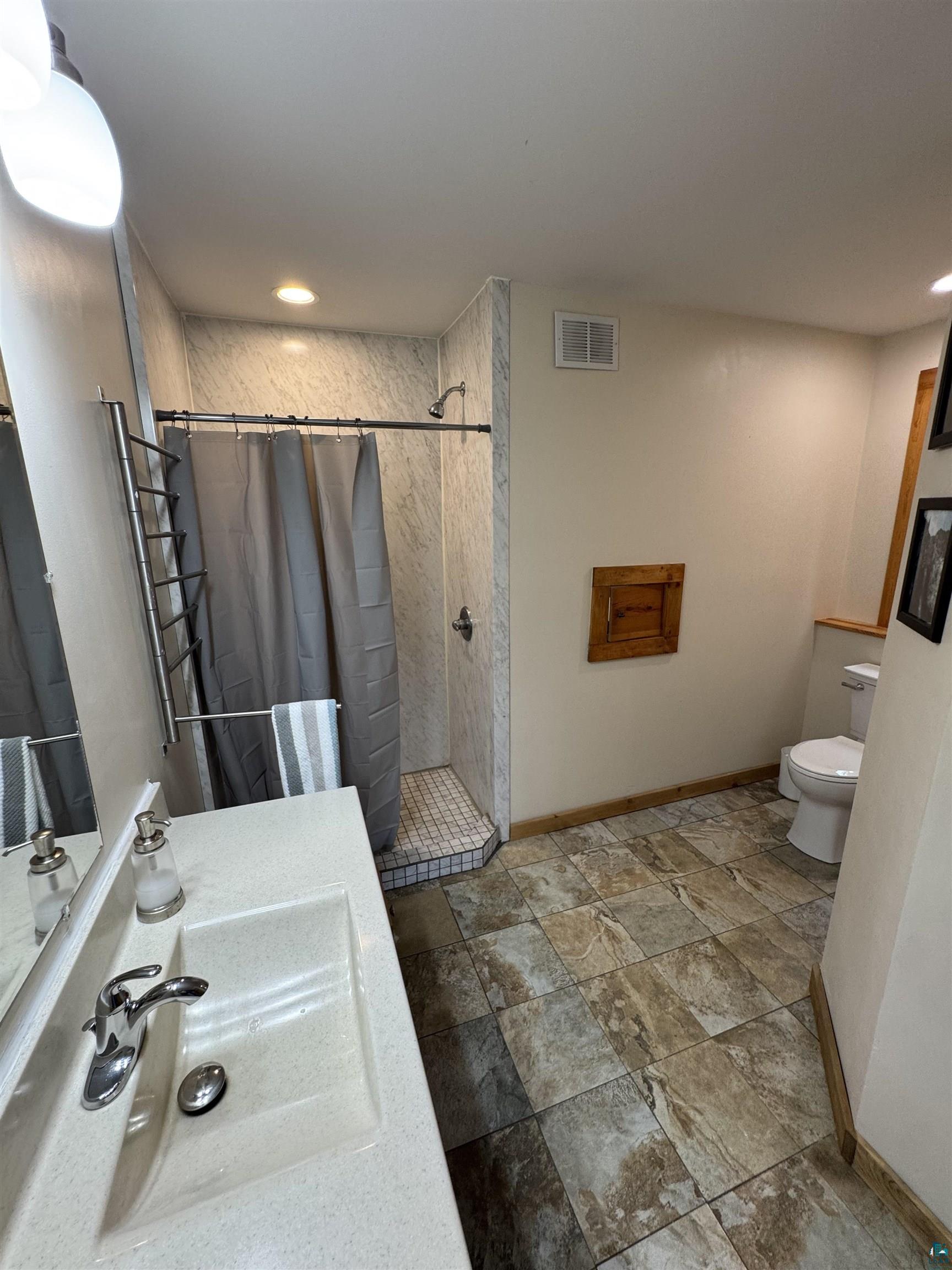 1745 Becks Road Maple, WI 54854 - Photo 20 of 46 Contemporary bathroom featuring a walk-in shower with tile surround, a single vanity with an integrated sink and chrome faucet, and patterned floor tiling