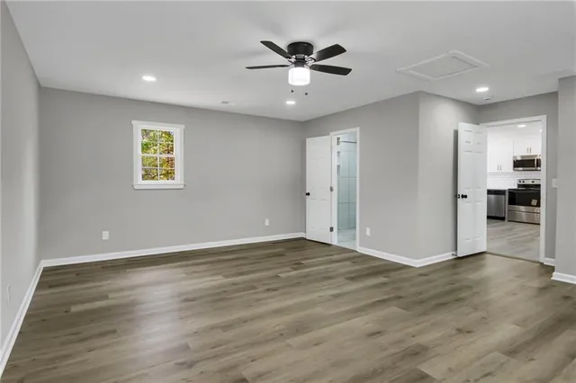 a view of an empty room with wooden floor and a ceiling fan