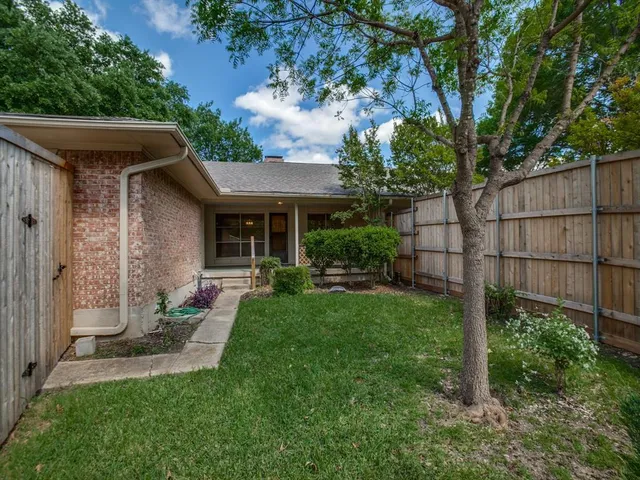 a view of a house with a yard plants and large tree