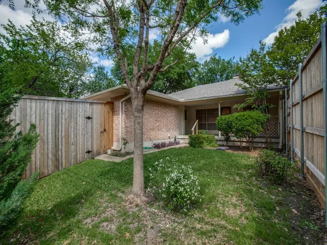 a view of a house with a yard plants and large tree