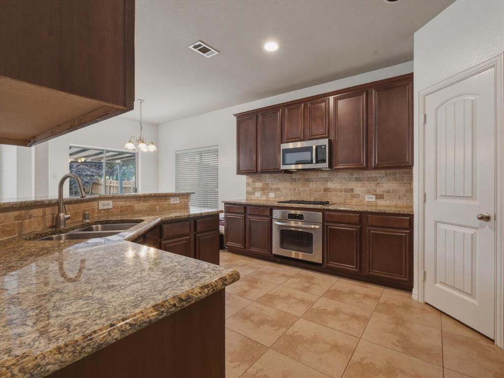 2364 Ranchview Drive Little Elm, TX 75068 - Photo 10 of 33 Kitchen featuring dark wood cabinetry, light granite countertops, stainless steel appliances, and a tiled backsplash