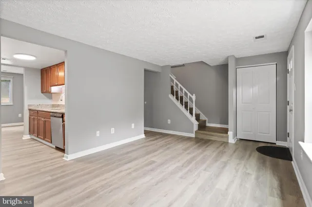 a view of an empty room with wooden floor and a kitchen