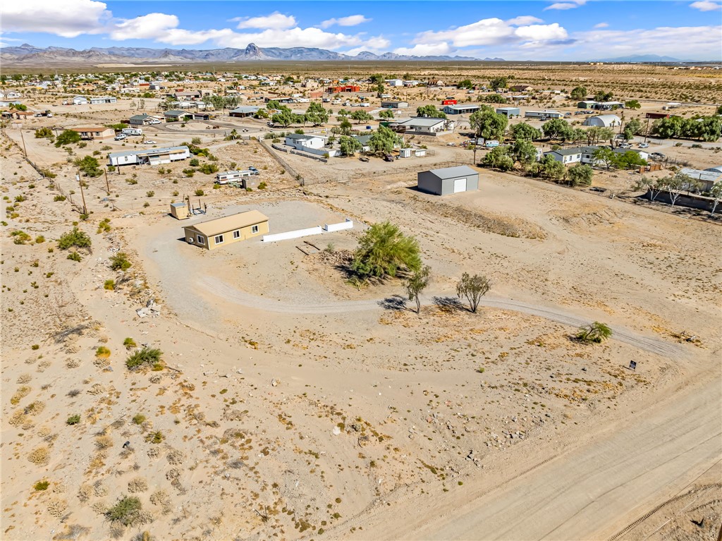 Aerial perspective showcasing a single-story residence with a light-toned exterior, a detached metal outbuilding, and expansive arid terrain