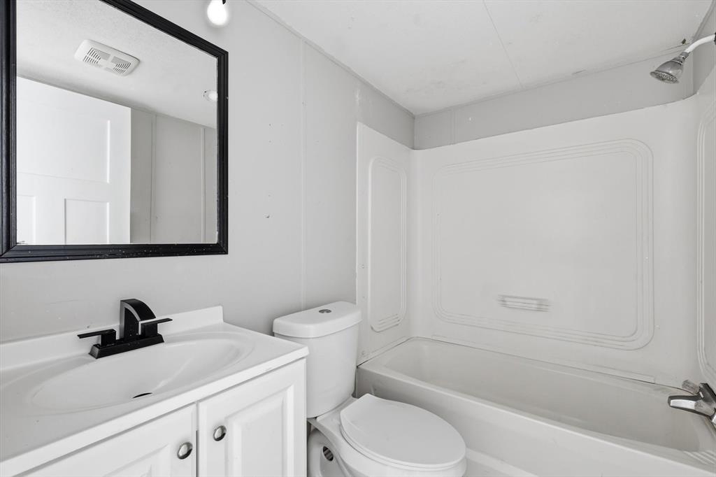 316 Summit Drive Springtown, TX 76082 - Photo 28 of 39 The bathroom features a vanity with a white countertop and sink, a black framed mirror, and a bathtub with a shower head